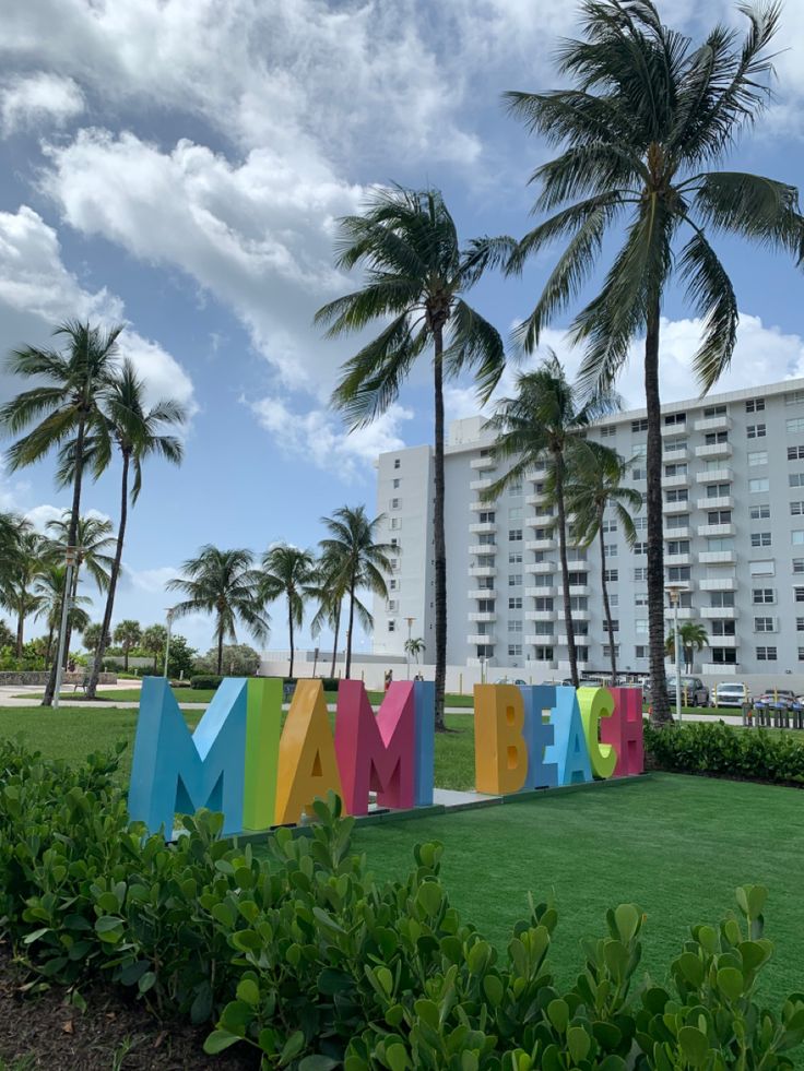 the word miami spelled out in multicolored letters with palm trees behind it on a sunny day