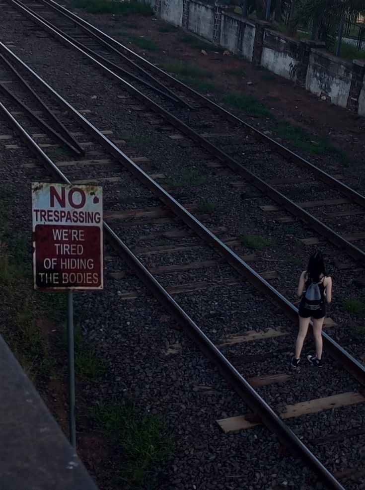 a woman standing on train tracks next to a no trespassing sign