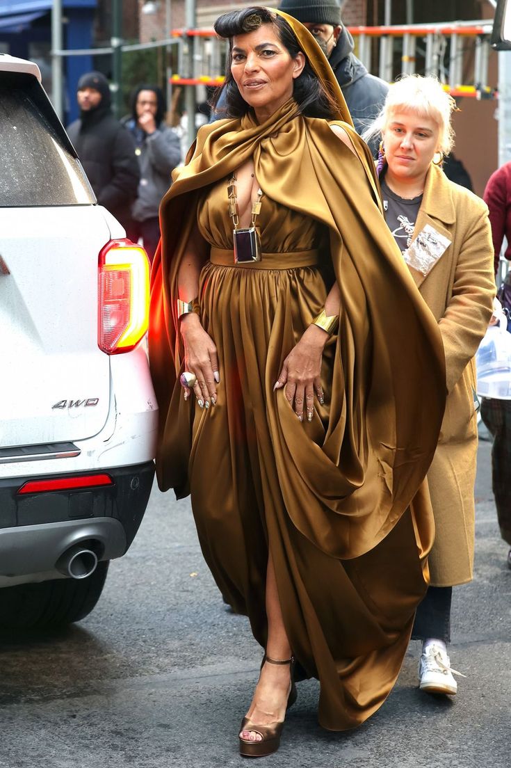 a woman in a brown dress is walking down the street with her hand on her hip