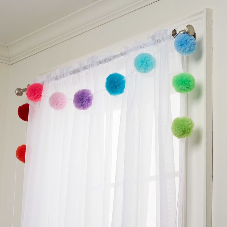 colorful pom - poms are hanging on the curtain in front of a window