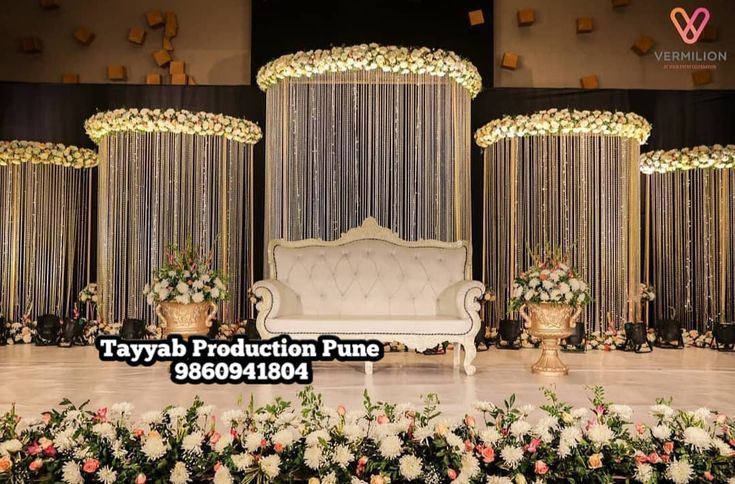 a white couch sitting on top of a stage covered in flowers and greenery next to gold vases