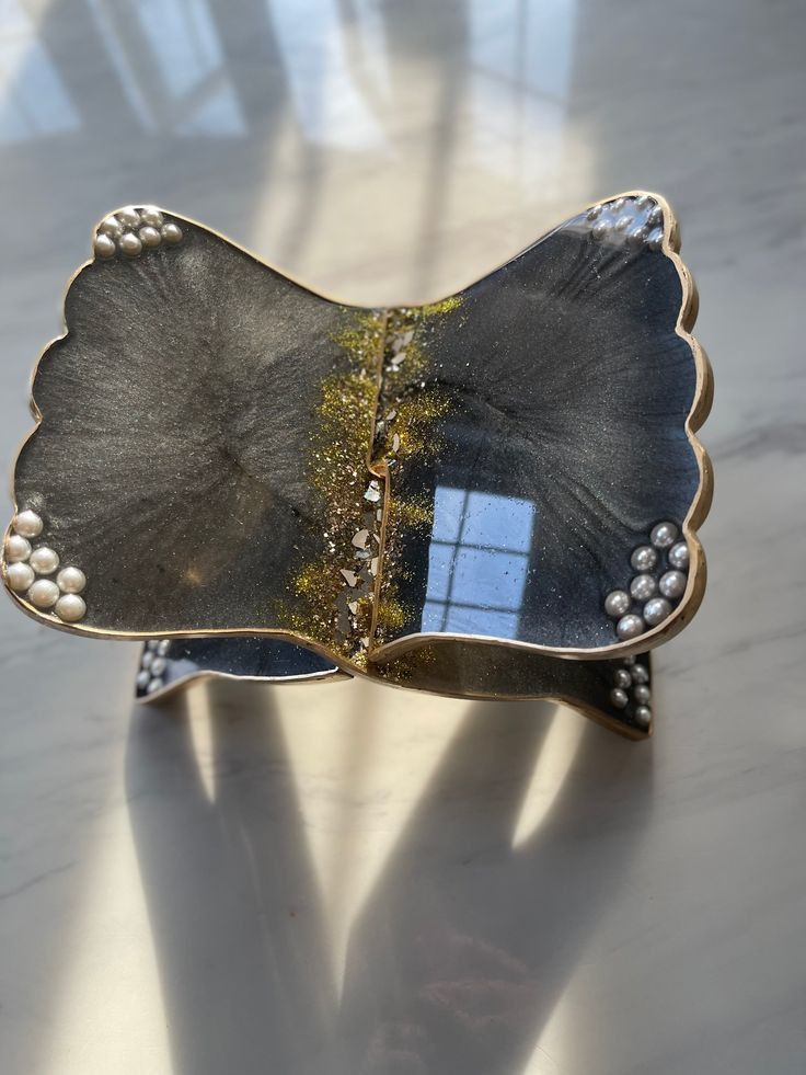 a silver and gold leaf shaped broochle with pearls on the sides, sitting on a table