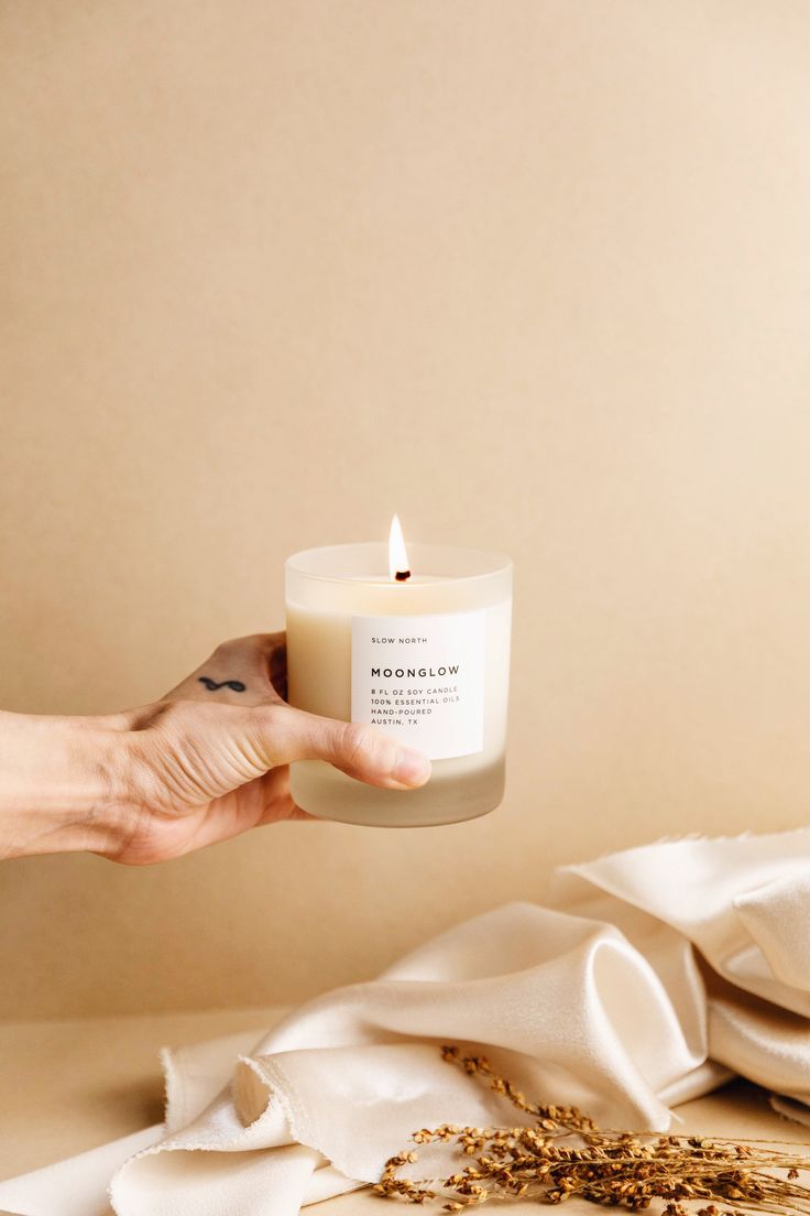 a person holding a candle in front of a white cloth on a table with other items