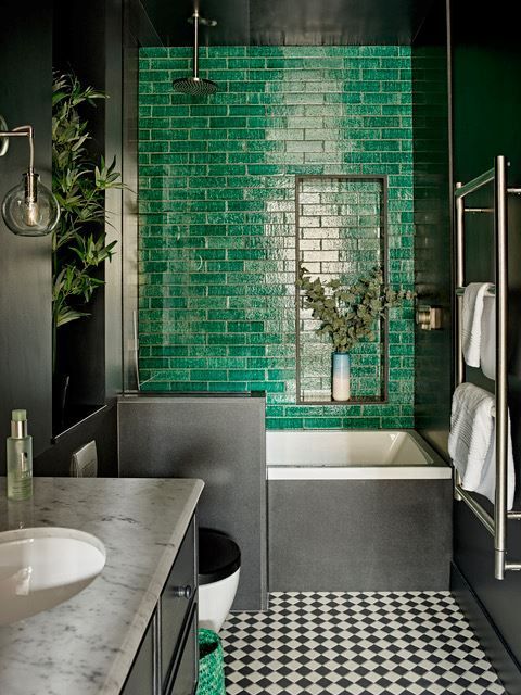 a bathroom with black and white checkered flooring, green brick wall and tub