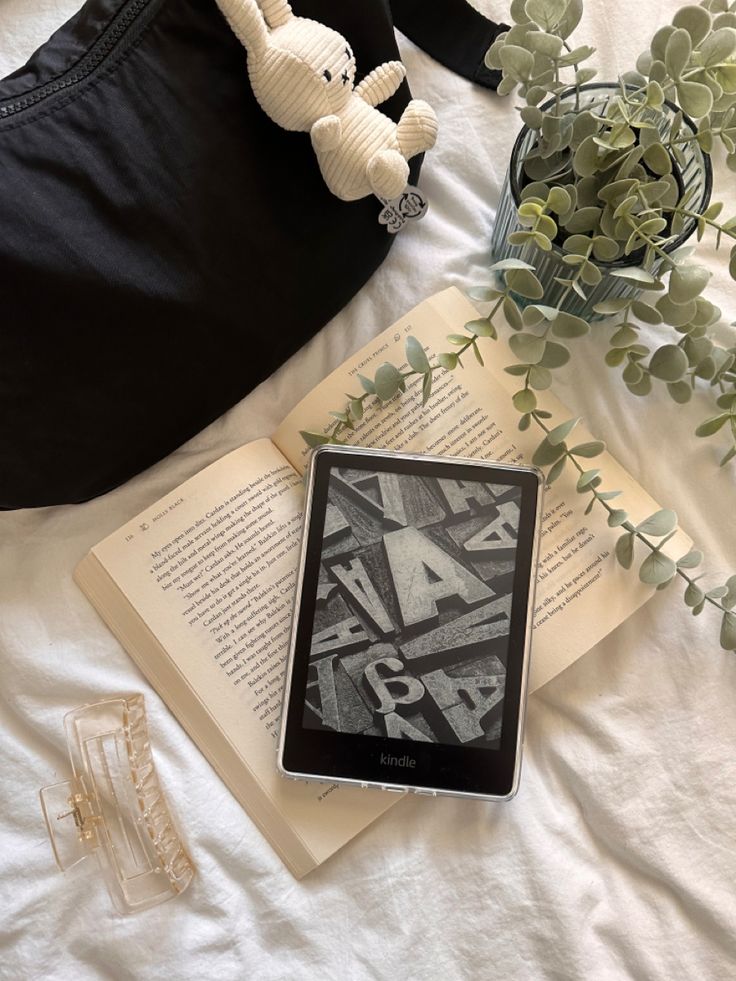 an open book sitting on top of a bed next to a stuffed animal and plant