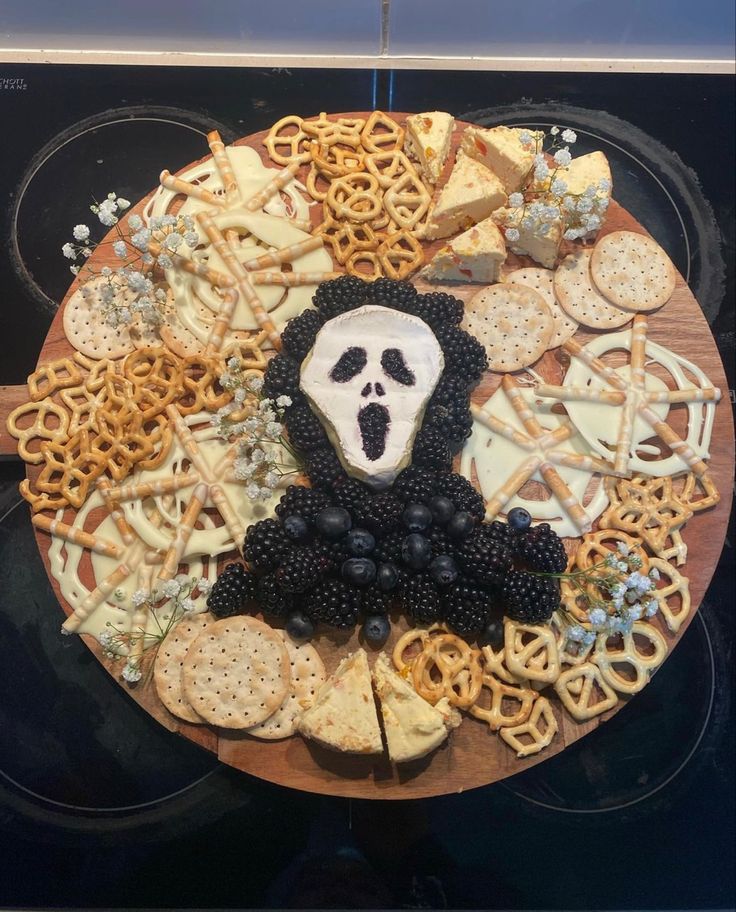 a platter filled with cheese, crackers and blackberries in the shape of a skeleton