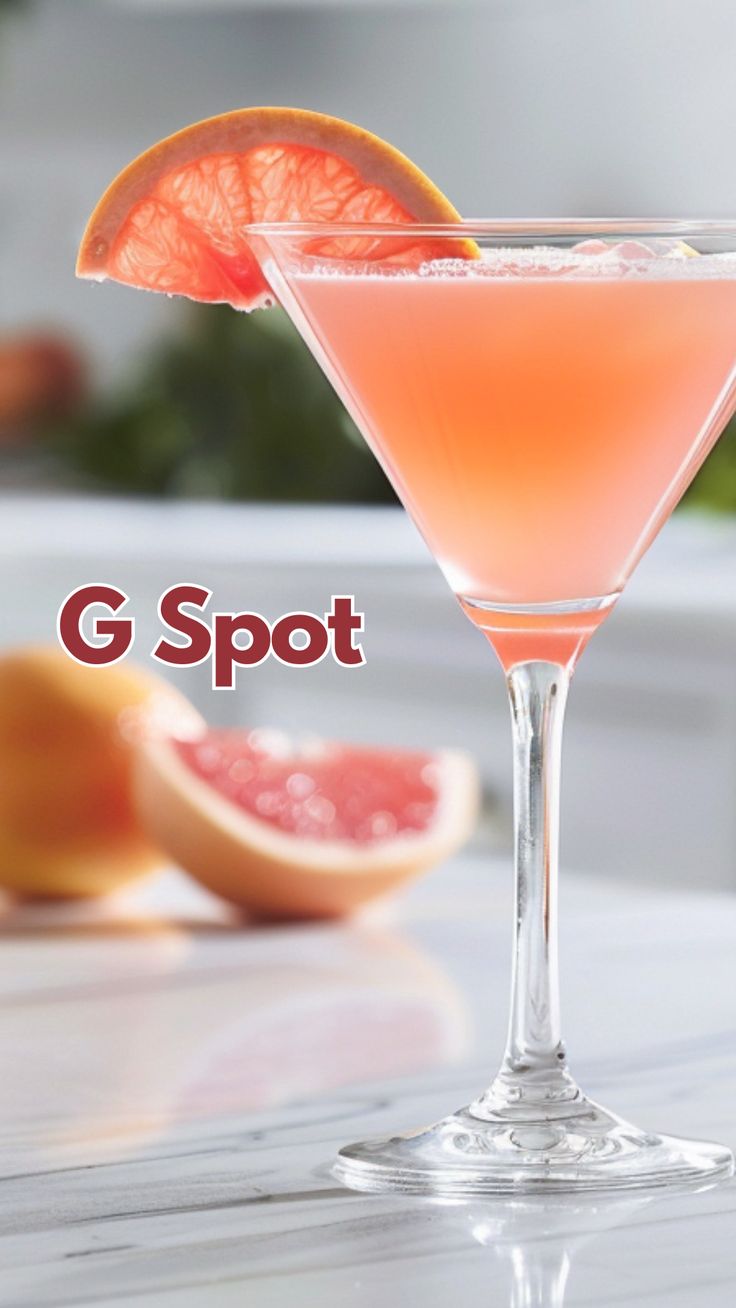 a pink cocktail garnished with grapefruit and an orange slice on the side