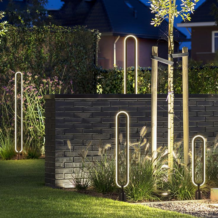 an outdoor garden area with various plants and decorative metal objects in the grass, along with a brick wall