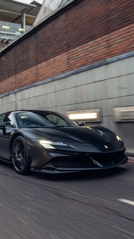 a black sports car driving down the road in front of a brick wall and building