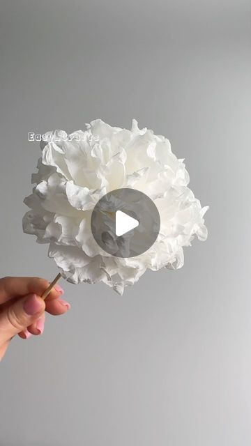 a person is holding a white flower with a video in front of them that reads, how to make paper flowers