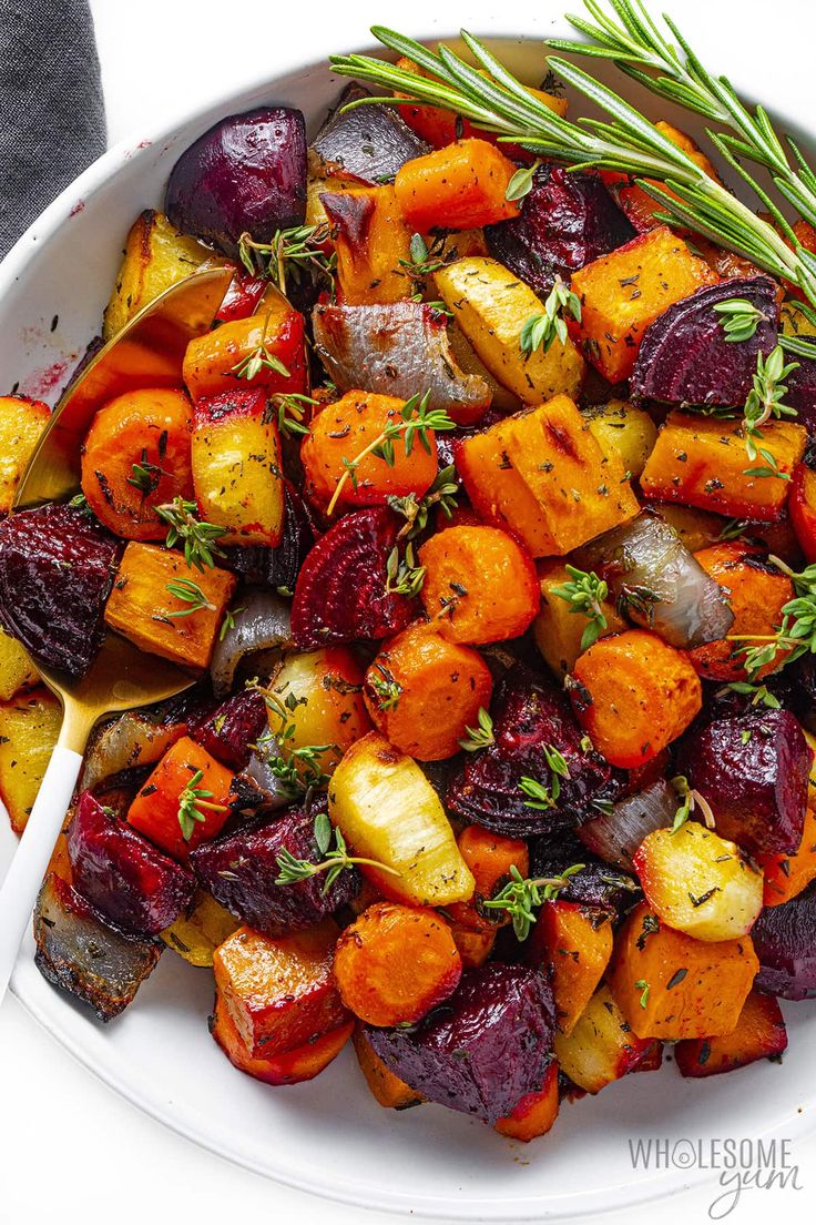 a white bowl filled with roasted beets, potatoes and rosemary garnishes