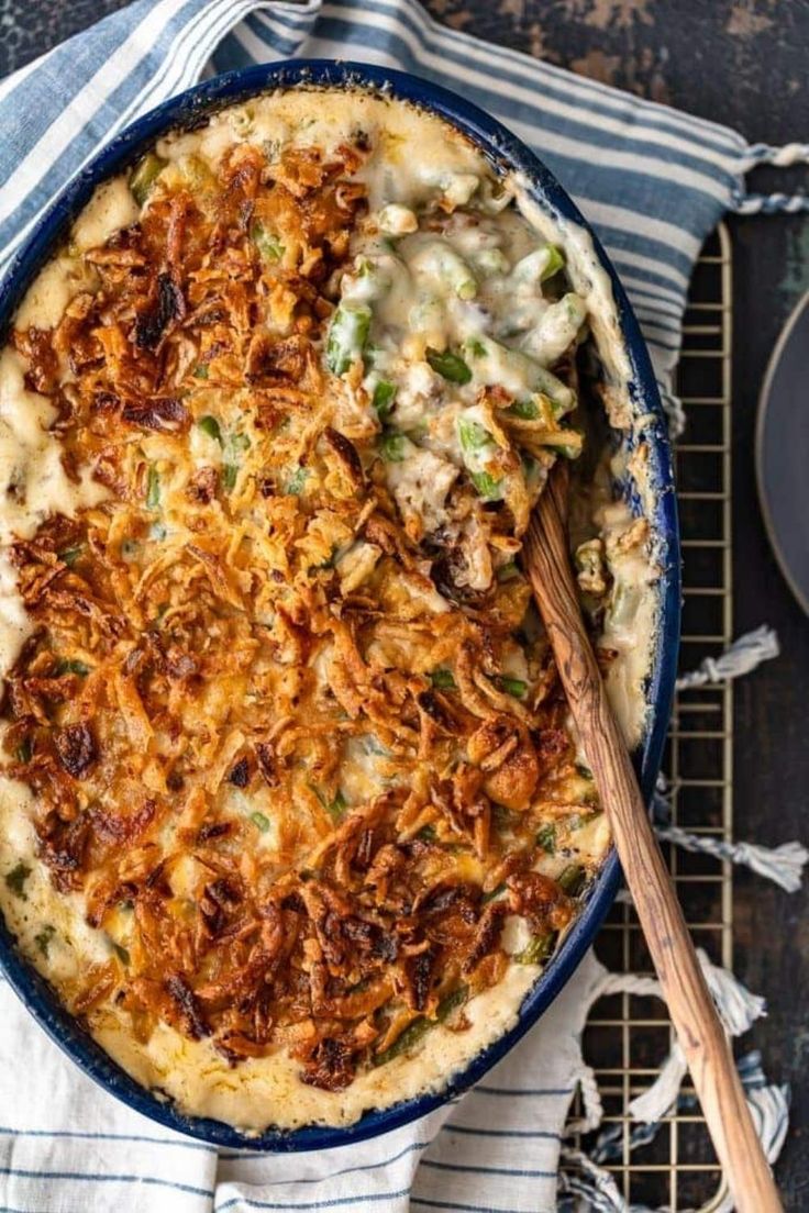 a casserole dish with cheese and vegetables in it on a cooling rack next to a wooden spoon