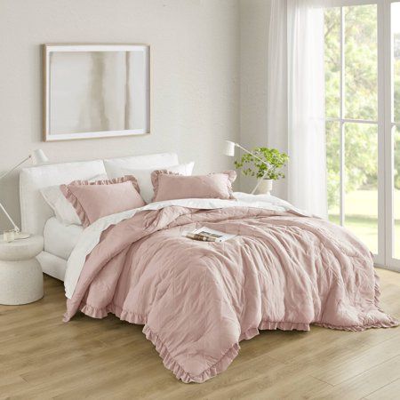 a bed with pink comforter and pillows in a white room