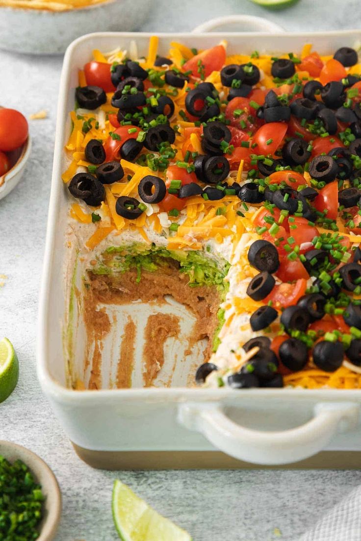 a white casserole dish filled with black olives, tomatoes and green peppers