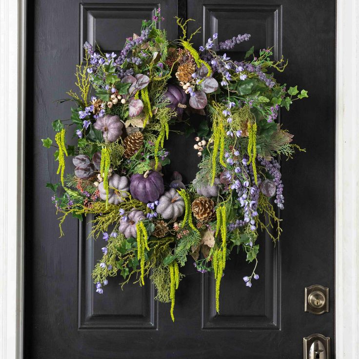 a wreath on the front door with purple flowers and greenery hanging from it's side