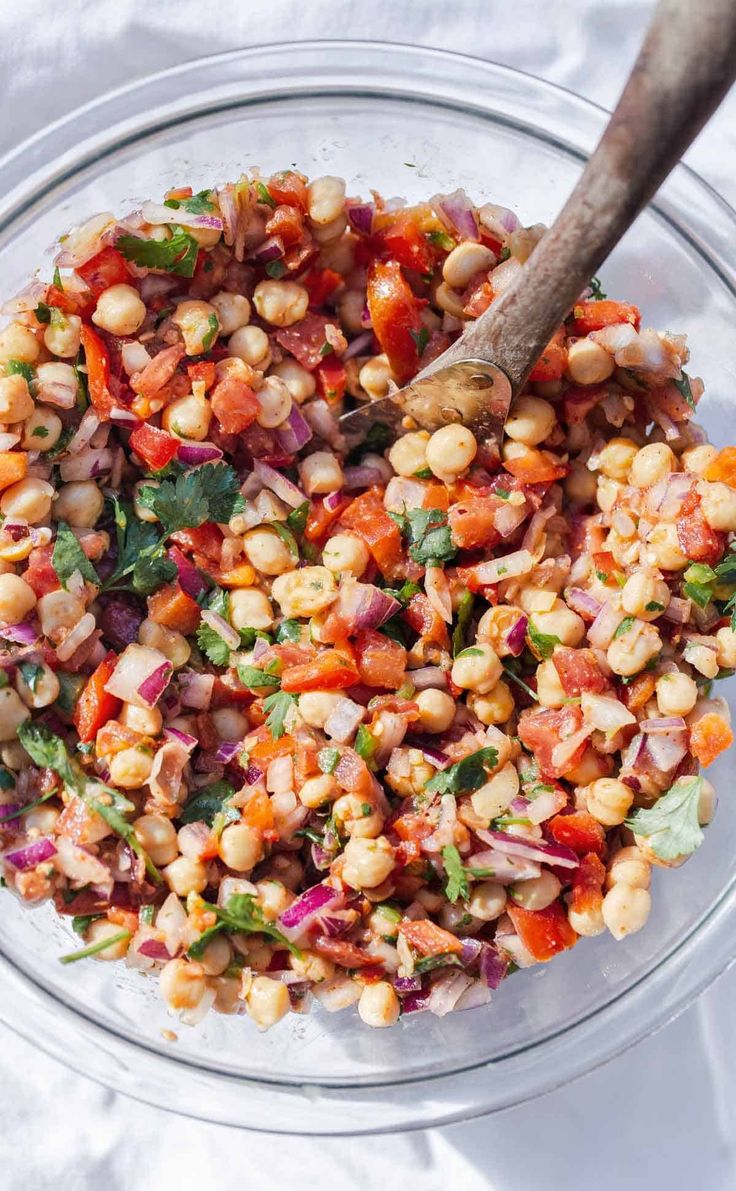 a glass bowl filled with chopped vegetables and a wooden spoon in the middle, on top of a white cloth