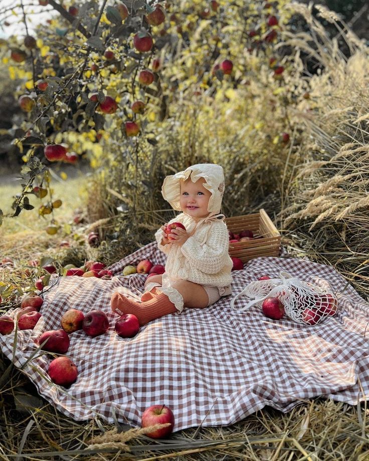 a baby sitting on a blanket in the middle of an apple orchard, eating apples