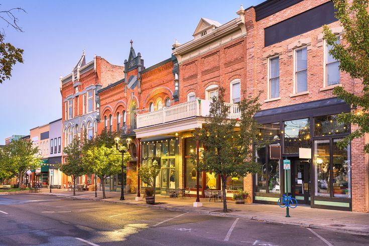 an empty street in the middle of town with shops on each side and trees lining both sides