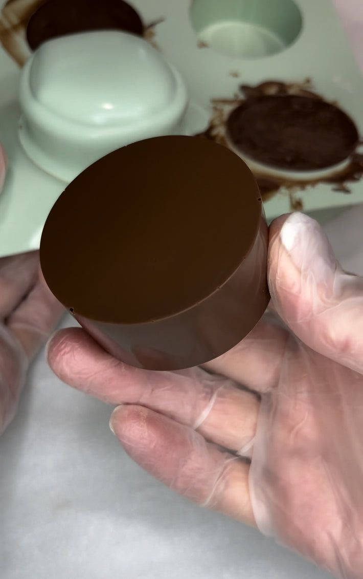 a person holding an empty chocolate cup in their hand with other items on the table behind them