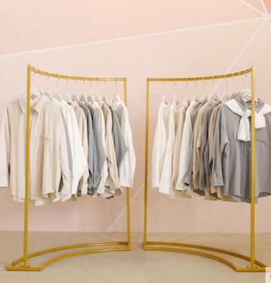 two racks with clothes hanging on them in front of a pink wall and white walls