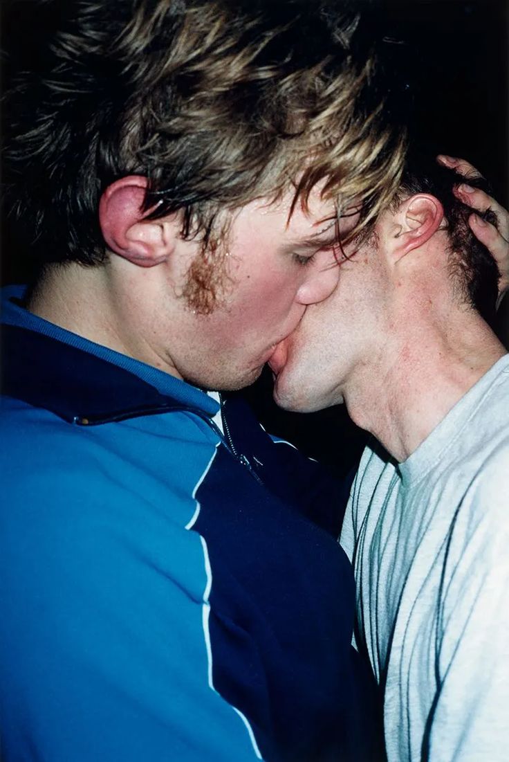 two men are kissing each other while one is wearing a blue shirt