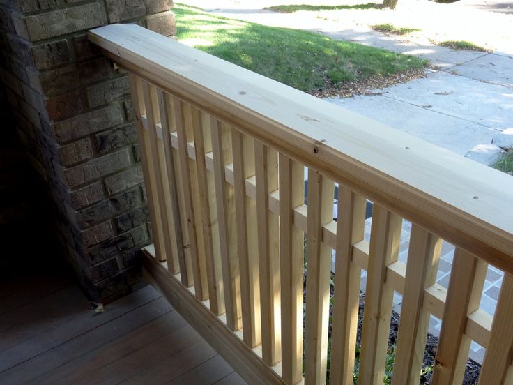 a wooden balcony railing next to a brick wall with grass and trees in the background