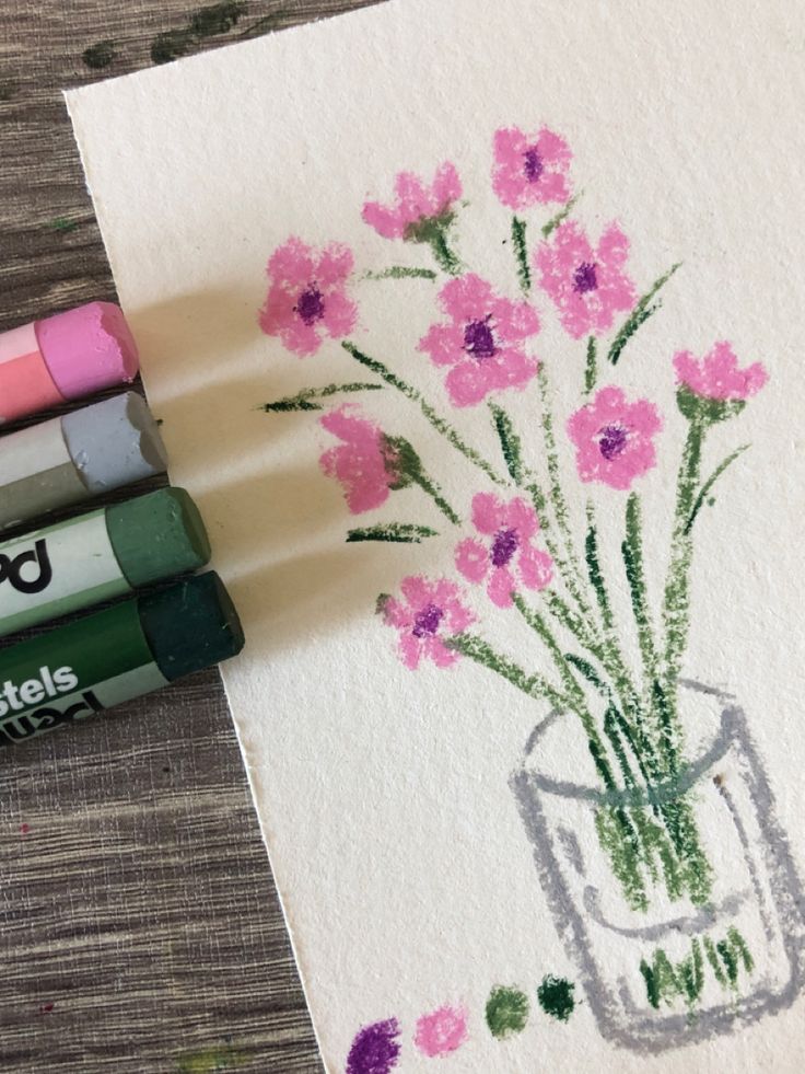 three crayons are next to some pink flowers in a vase on a piece of paper