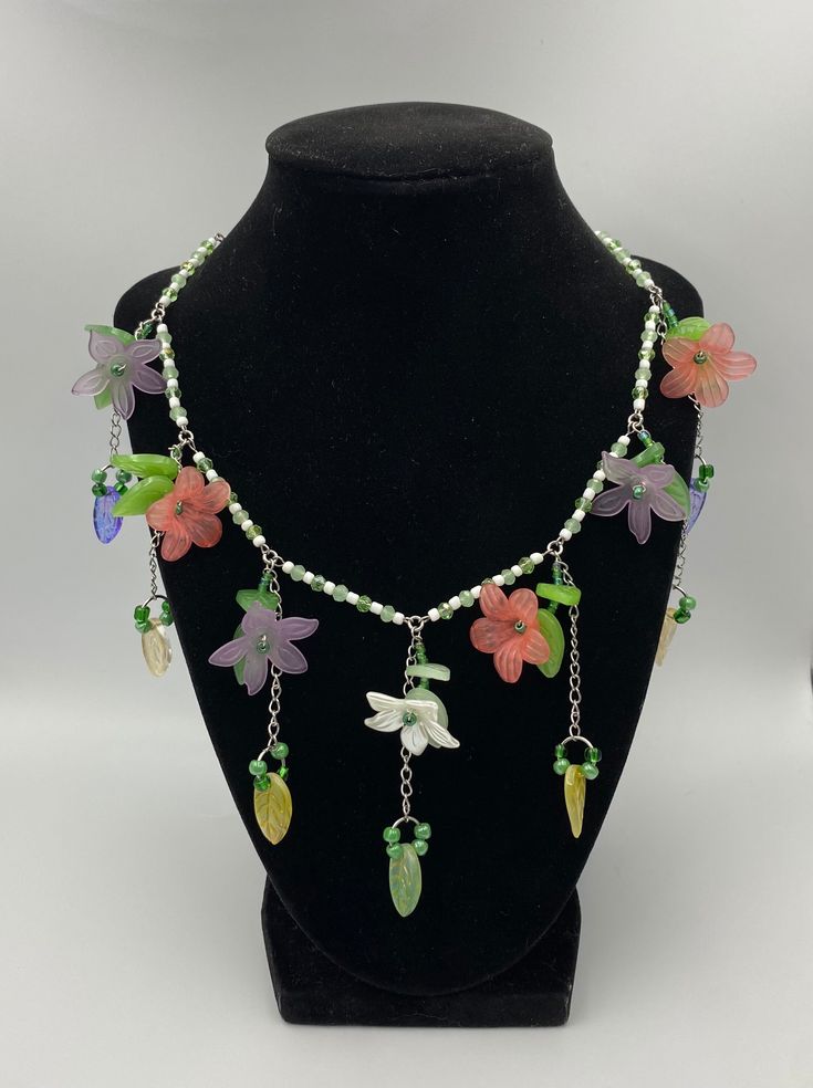 Handcrafted necklace with green and white beads, purple and pink flower charms with leaves adjustable length 17.5-20 inches Whimsical Green Flower Jewelry, Whimsical Handmade Green Beaded Necklaces, Green Adjustable Necklace With Flower Charm, Adjustable Whimsical Green Necklace, Green Bohemian Flower Charm Necklace, Green Flower Necklace With Colorful Beads, Whimsical Green Necklace, Adjustable Green Flower Necklace, Handmade Multicolor Fairycore Jewelry