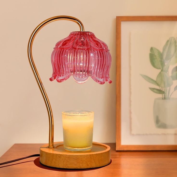 a pink lamp sitting on top of a wooden table next to a glass candle holder