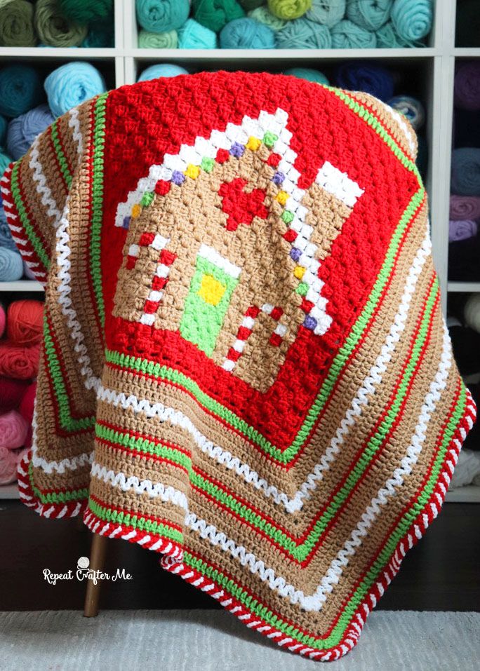 a crocheted blanket with a gingerbread house on it in front of some yarns