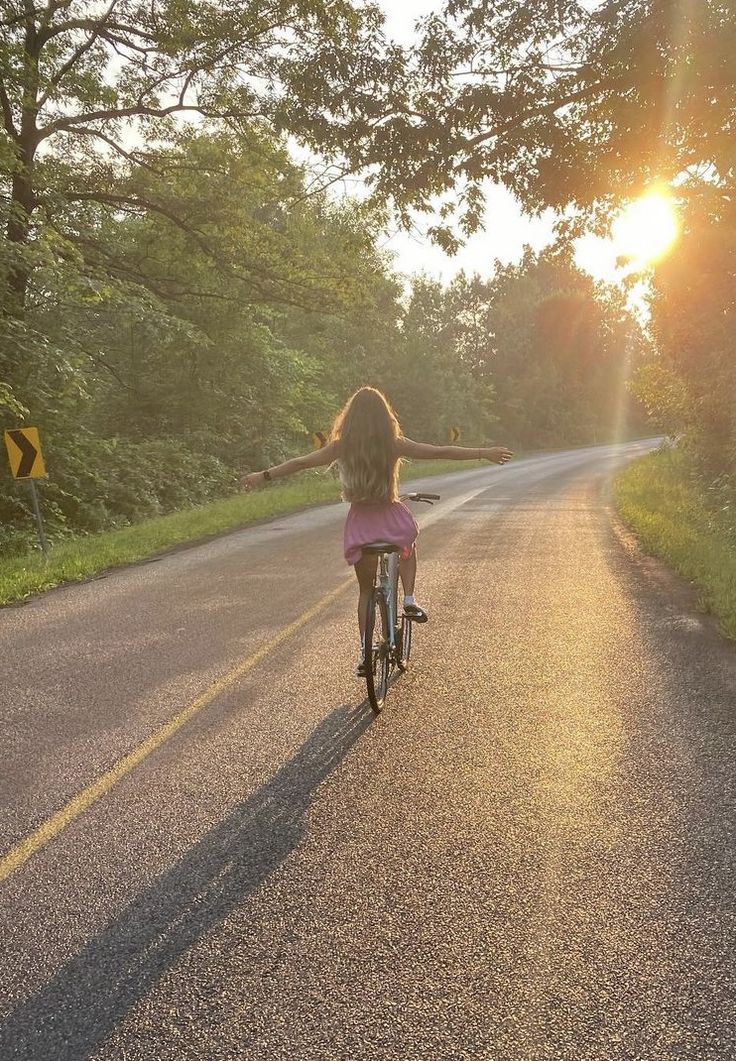 a woman riding a bike down the middle of a road with her arms spread out