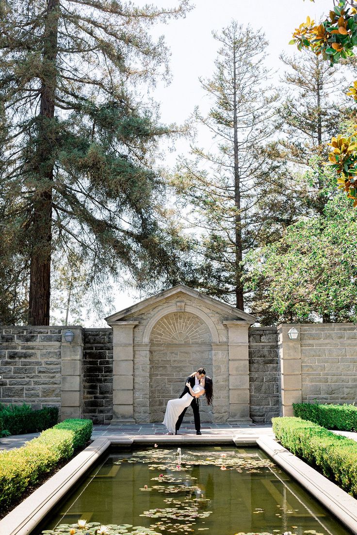 a bride and groom standing in front of a pond at the end of their wedding day