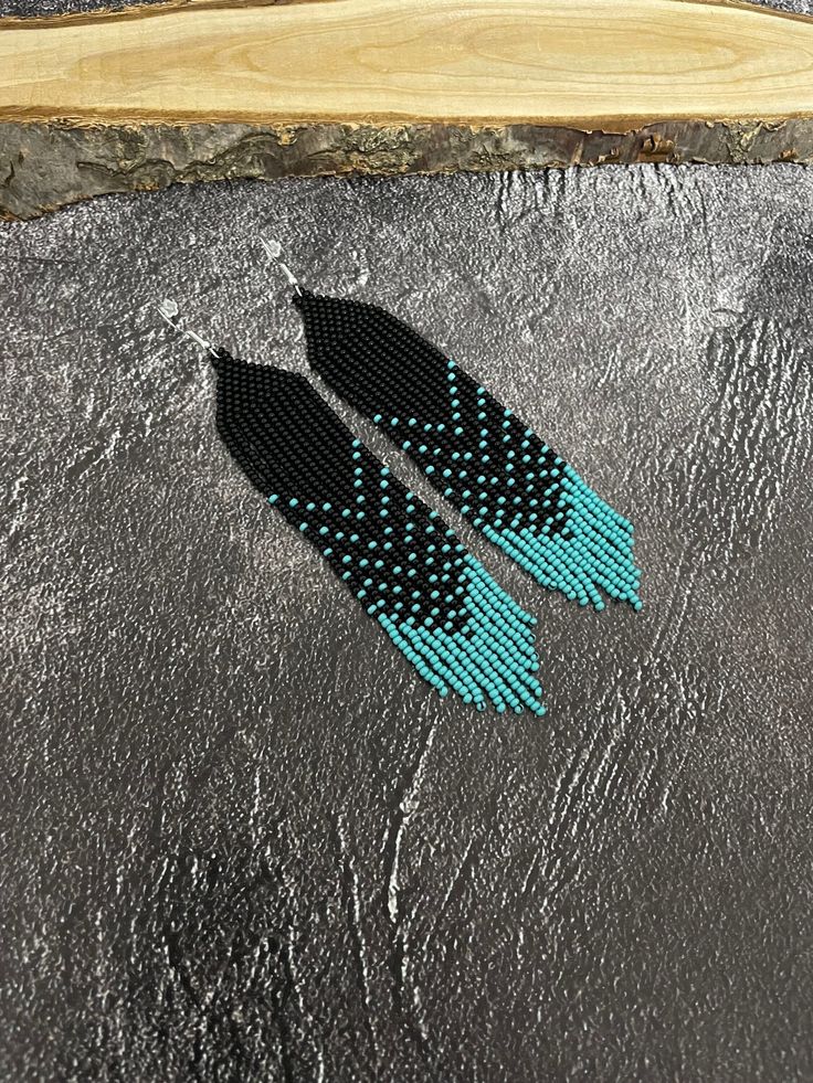 two black and blue beaded earrings sitting on top of a stone slab next to a piece of wood