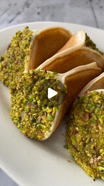 three tacos on a white plate covered in green and yellow toppings, sitting on a marble table