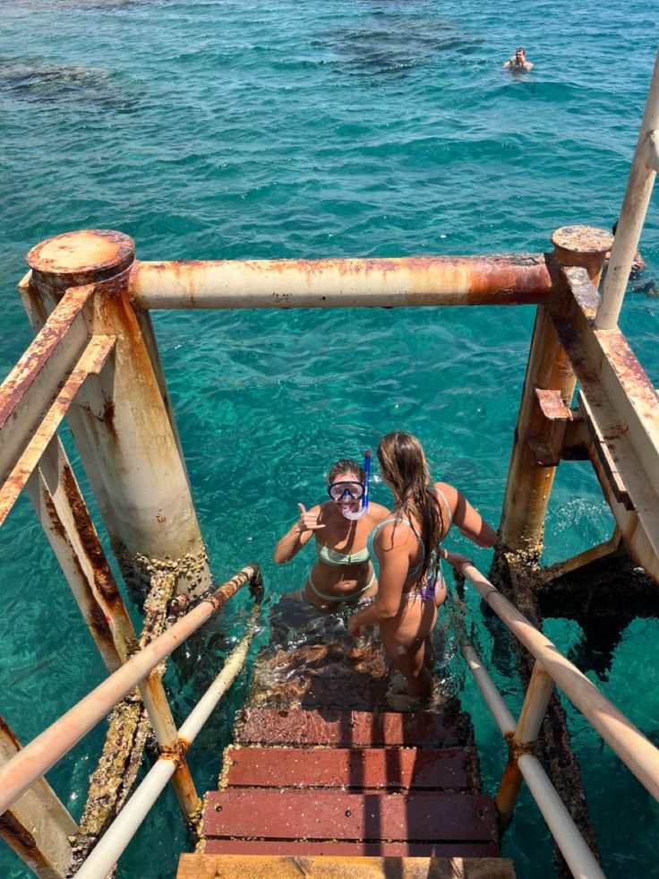 two women are standing on stairs in the water with their snorkels out