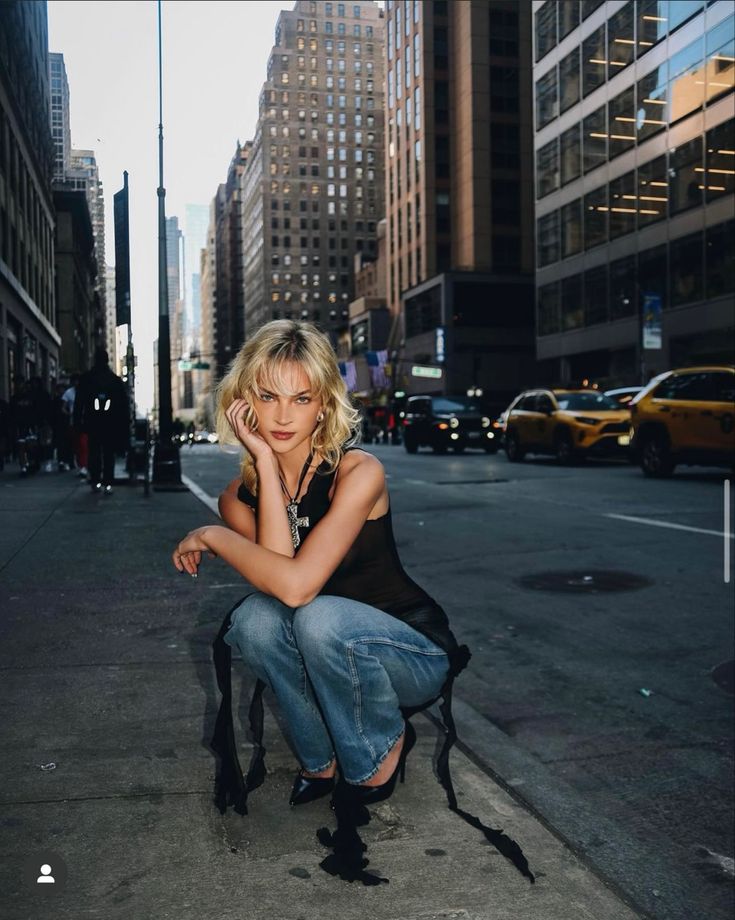 a woman sitting on a chair in the middle of an empty street with tall buildings behind her