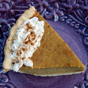 a slice of pumpkin pie with whipped cream on top sits on a purple plate, surrounded by blue swirls