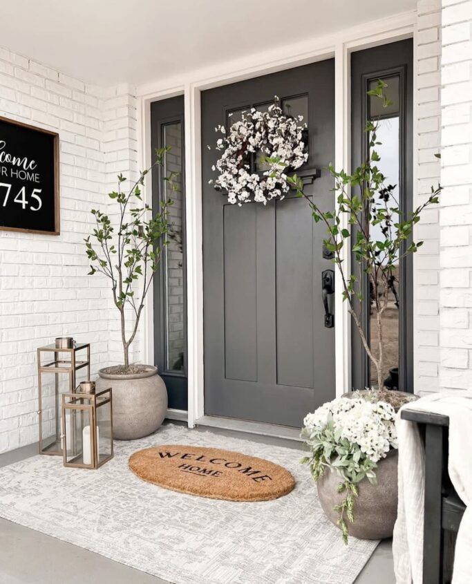 a welcome mat on the front door of a house with potted plants and lanterns