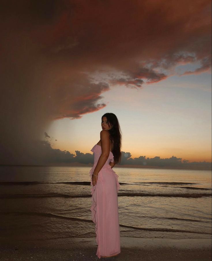 a woman standing on top of a beach next to the ocean under a cloudy sky