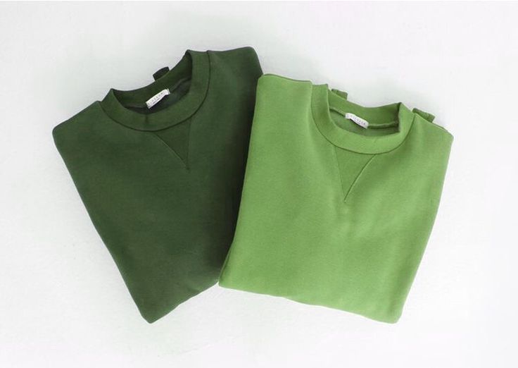 two green sweatshirts sitting next to each other on a white surface with no background