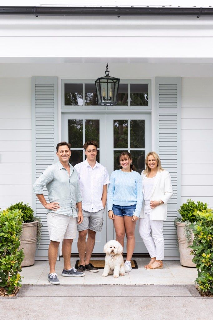 a group of people standing in front of a white house with a dog on the porch