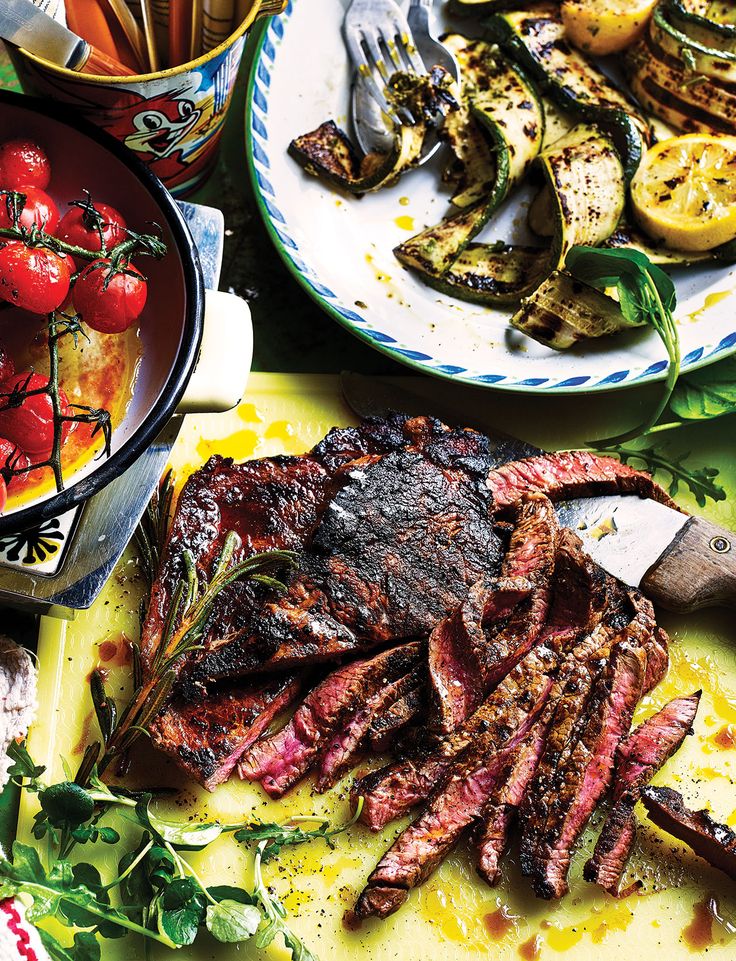 steak, tomatoes and other vegetables on a table with utensils in the background