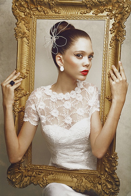 a woman in a white dress holding up a gold frame