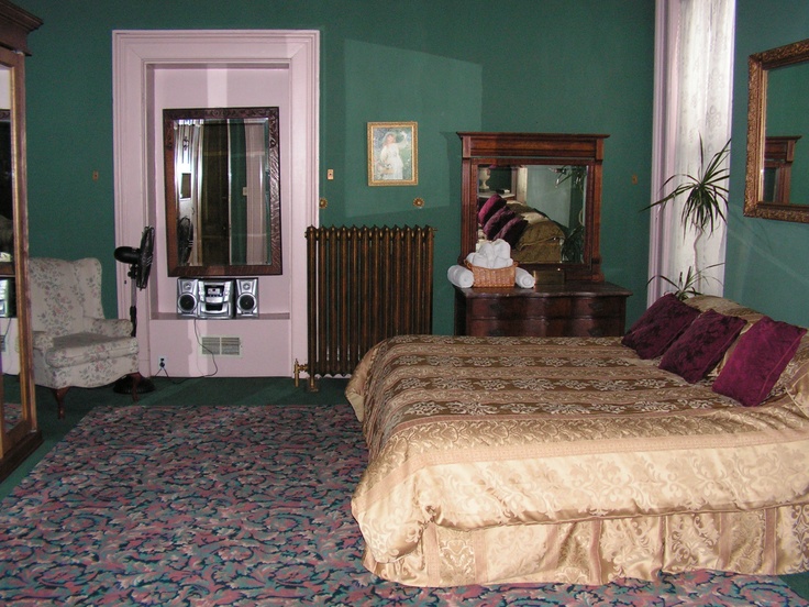 a bed room with a neatly made bed next to a chair and mirror on the wall