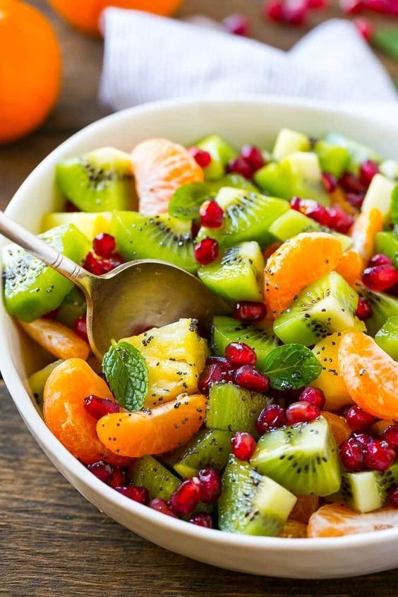 a fruit salad with kiwi, oranges and pomegranate in a white bowl