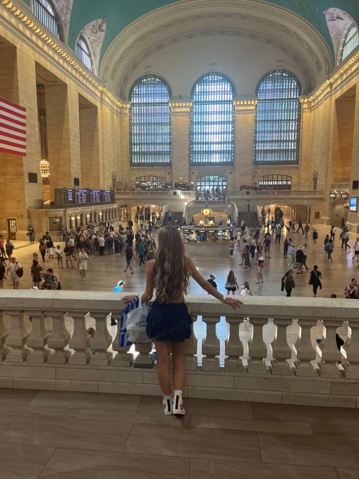 a woman standing on a balcony looking at people in an indoor area with large windows