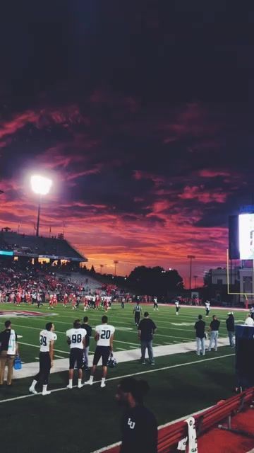 a group of people standing on top of a football field at night with the sun going down