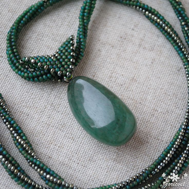 a necklace with green beads and a large stone pendant on it's end, sitting on a piece of fabric