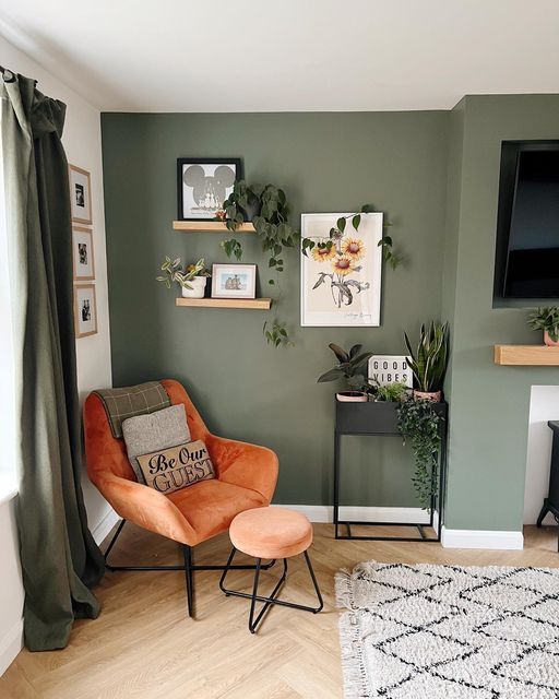 a living room with green walls and orange chairs in front of a fire place mantle