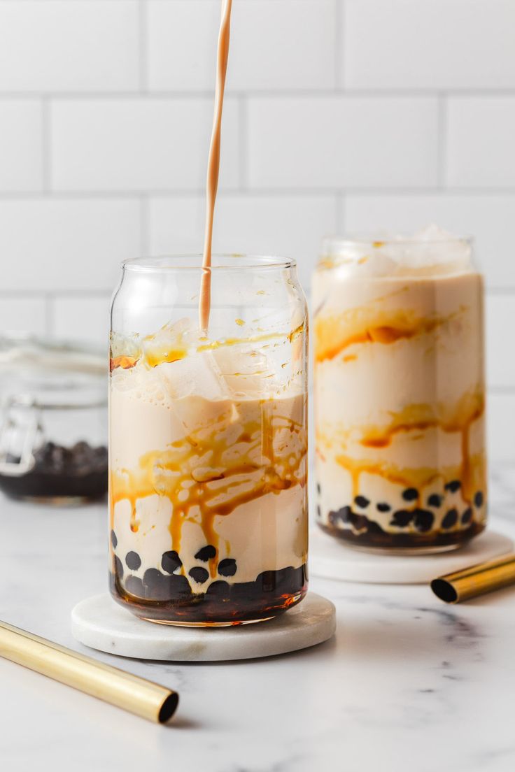 two jars filled with desserts sitting on top of a counter next to gold utensils